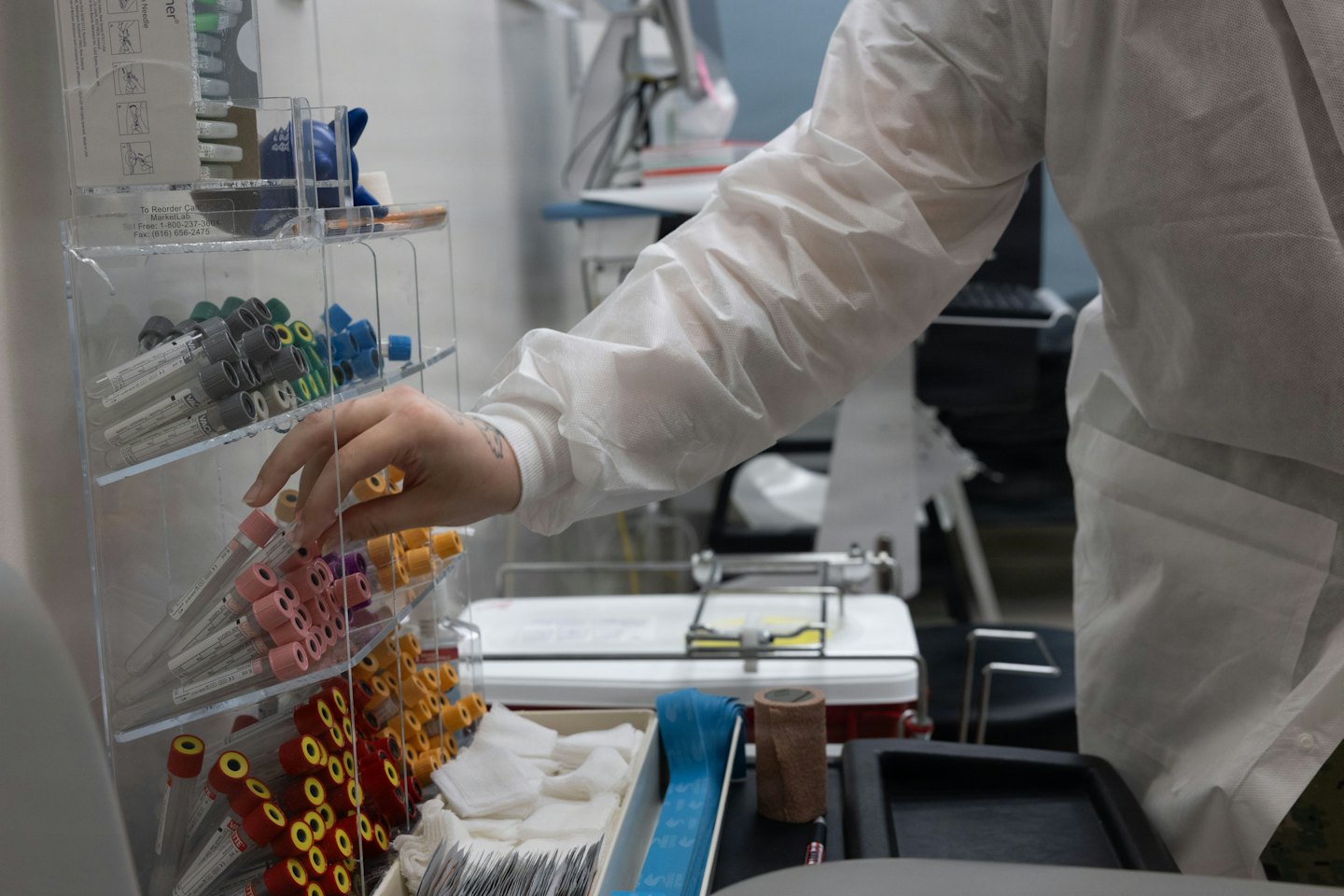Healthcare worker in a lab coat selecting a blood tube.